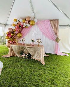 a table with gold, pink and white balloons on it under a tented area