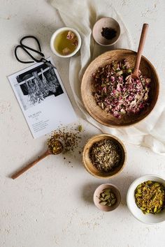 bowls filled with different types of herbs on top of a white tablecloth next to two spoons