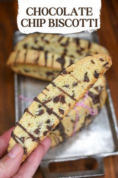 chocolate chip biscotti is being held up in front of a metal tray with the title