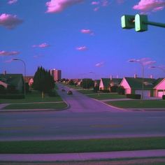 an empty street with houses in the background and a green traffic light on one pole