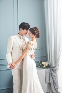 a bride and groom standing next to each other in front of a blue wall holding hands