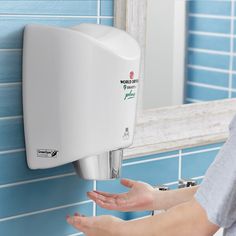 a person holding their hand out towards a white urinal on a blue tiled wall