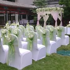 rows of white chairs with green sashes and flowers on them in front of a building