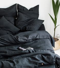 a bed with black linens and pillows on it, next to a potted plant