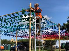 a man standing on top of a ladder next to a wooden structure covered in kites