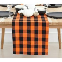 an orange and black plaid table runner with white pumpkins on the top, next to plates