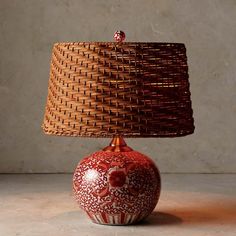 a red and white vase with a brown lamp shade on it's head sitting on a table