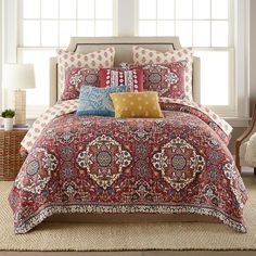 a red and blue bed in a bedroom next to a window with two lamps on either side