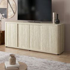 a flat screen tv sitting on top of a wooden cabinet in front of a wall mounted clock