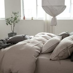 an unmade bed with several pillows and blankets on it in front of two windows