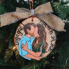 a christmas ornament hanging from a tree with a couple hugging each other on it