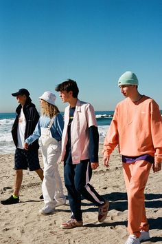 four people walking on the beach with one person wearing an orange shirt and white hat