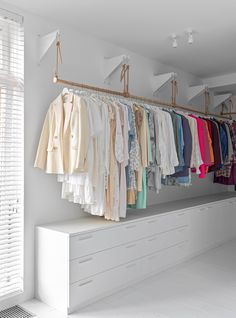 a closet filled with lots of clothes next to a white window covered in shutters