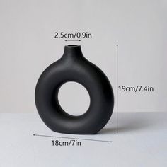 a black vase sitting on top of a table next to a white wall with measurements