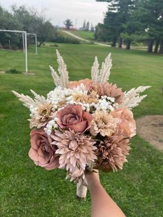 a bouquet of flowers in someone's hand on the grass near a soccer field