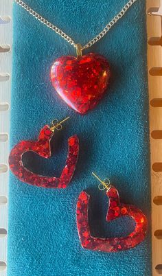 Standout with this vibrant red heart pendant and open heart post back earrings. 18" gold nickle free iron curb chain, 2mm. Lobster clasp closure. Earrings have gold hypoallergenci posts. Made with epoxy resin and red chunk glitter. Handcrafted items often have slight imperfections which are part of the creative process and add to the character of the piece; no 2 are alike!  Colors you see on the screen may differ slightly from in person due to variations in lighting, camera and electronic postin Trendy Red Jewelry With Heart Beads, Red Heart Pendant Earrings, Valentine's Day Party Heart Earrings With Open Heart Shape, Trendy Red Heart-shaped Jewelry, Trendy Red Heart Earrings For Valentine's Day, Red Heart Beads Earrings For Gift, Valentine's Day Heart-shaped Resin Jewelry, Red Heart Pendant Earrings For Valentine's Day, Heart-shaped Resin Jewelry For Valentine's Day