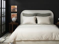 a bed with white sheets and pillows in a black room next to a large window