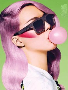 a woman with pink hair and sunglasses blowing a bubble