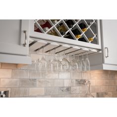 wine glasses and bottles are hanging on the wall above the kitchen cabinets in this image