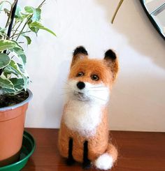 a needle - felt fox sits next to a potted plant on a wooden table