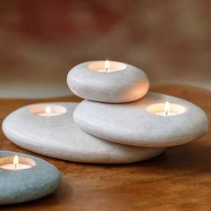 three lit candles sitting on top of some white rocks in the middle of a wooden table