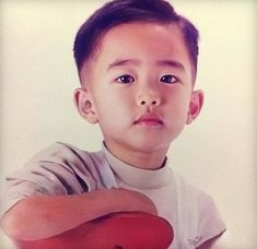 a young boy holding a red object in his right hand and looking at the camera