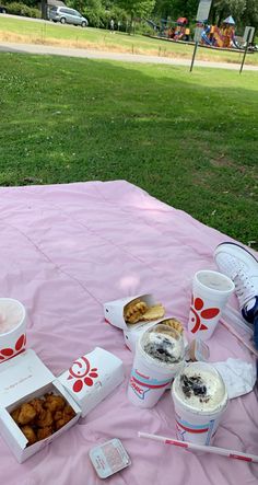 a picnic table with food and drinks on it in front of a grassy area at a park