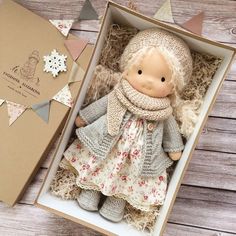 a small doll in a box on a wooden table next to a card and envelope