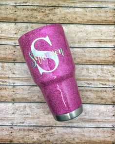 a pink glitter tumbler with the letter s on it sitting on a wooden surface