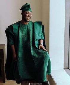 a man sitting on top of a wooden bench wearing a green dress and head scarf