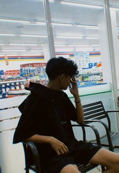 a person sitting on a bench talking on a cell phone in a store with shelves behind them