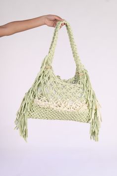 a hand holding a crocheted bag with tassels