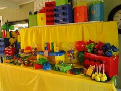 a yellow table topped with lots of toys and cake next to a wall mounted clock