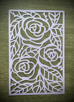 an intricate paper cut design with flowers and leaves on the edges is shown in white