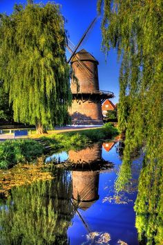 a windmill sitting on top of a lush green field next to a river filled with water