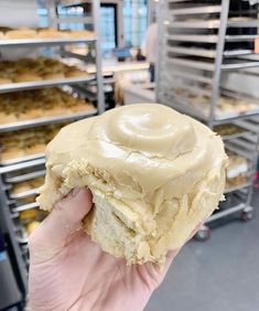 a person holding up a frosted doughnut in front of some baking racks