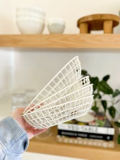 a person holding a white wire basket in their hand and some books on the shelf behind them