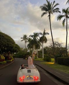 a bride and groom are riding in the back of a convertible car through palm trees