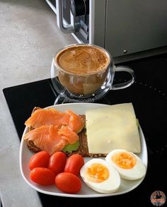 a white plate topped with eggs, tomatoes and toast next to a cup of coffee