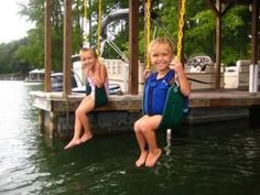 two young children sitting on swings in the water