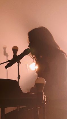 a woman sitting at a table with a microphone in her hand and the light behind her