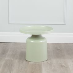 a light green stool sitting on top of a hard wood floor next to a white wall