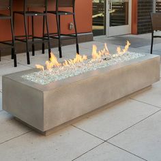 a fire pit sitting on top of a cement slab next to chairs and tables in front of an orange building