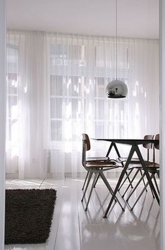 an open door leading to a dining room with white walls and curtains on the windowsill