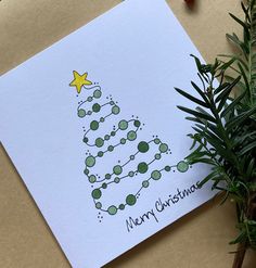 a card with a christmas tree drawn on it next to a potted green plant