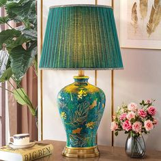 a green lamp sitting on top of a wooden table next to a vase with flowers