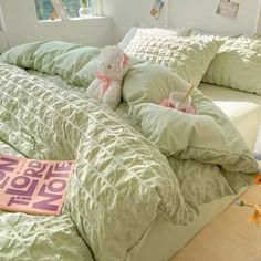 a bed with green comforter and pillows on it, next to a pink book