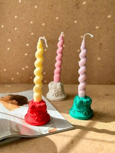 three candles sitting on top of a table next to an open book and candle holder