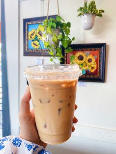 a person holding up a drink in front of a wall with pictures on it and a potted plant