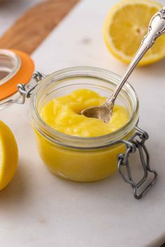 a spoon in a jar filled with lemon curd next to some sliced lemons